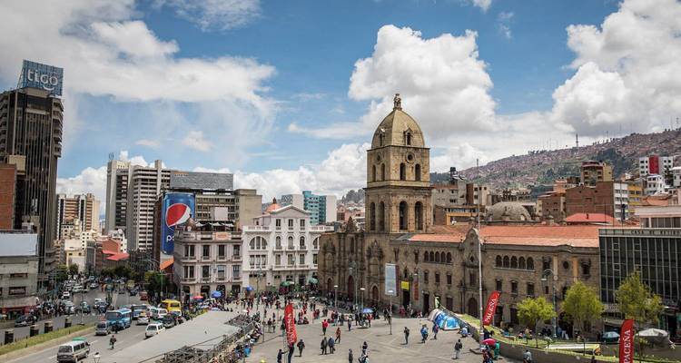 Bustling Plaza San Francisco with colonial church, modern buildings and crowds under a partly cloudy sky.