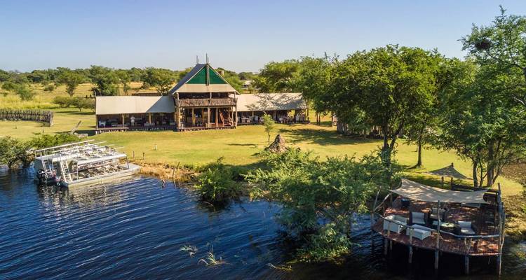 Riverside safari lodge with a moored double-deck boat and surrounding green lawns.