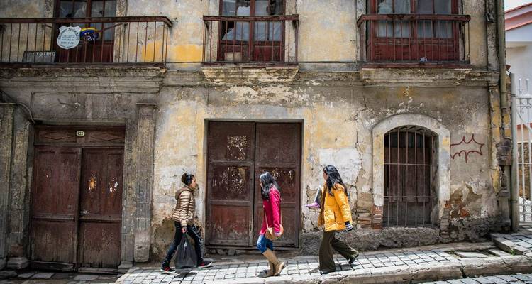 Three women walking past weathered colonial building on cobblestone street