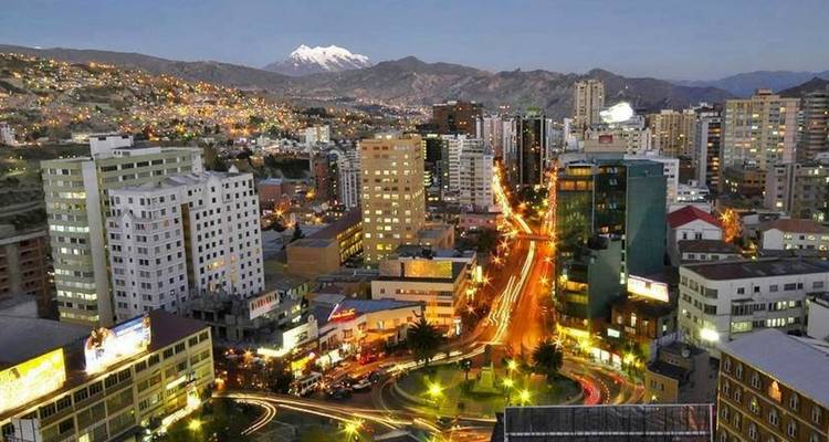 Night panorama of La Paz city lights with winding streets and snowy Illimani peak behind
