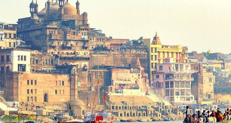 Panoramisch uitzicht op Varanasi's ghats en tempels die boven de Ganges uitrijzen met boten en pelgrims langs het water.