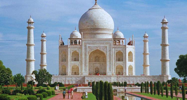 Het iconische witte marmeren Taj Mahal met minaretten rijst majestueus op onder een blauwe hemel, bezoekers wandelen in de tuinen eronder.
