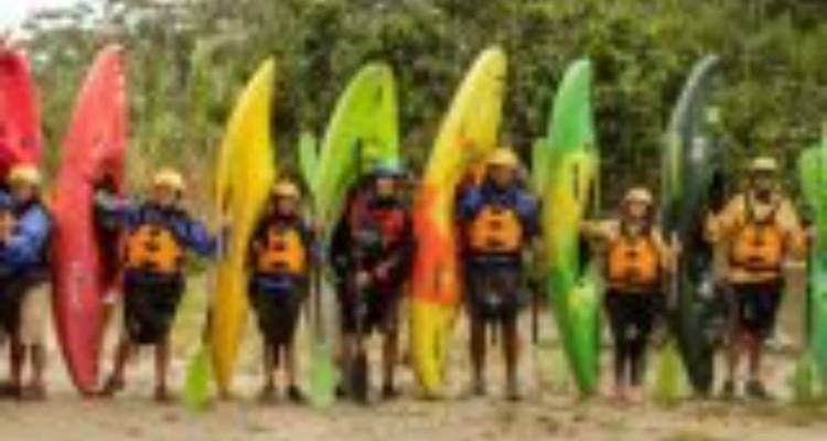 Blurry lineup of kayakers holding colorful kayaks on a riverbank.