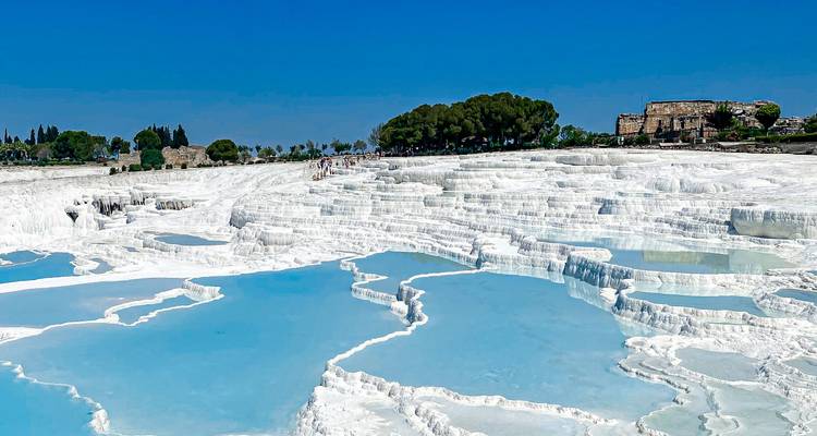 Vista expansiva de las deslumbrantes piscinas blancas de calcita de Pamukkale y agua azul contra un cielo de verano vívido.