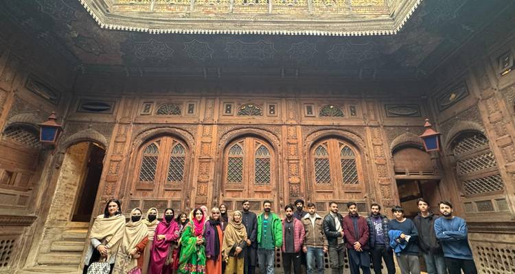 Grand groupe de voyageurs posant devant une cour en bois ornée d'un manoir historique.
