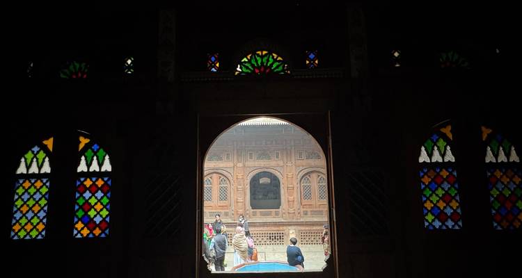 Vue à travers une porte voûtée avec des vitraux colorés vers des visiteurs dans une cour.