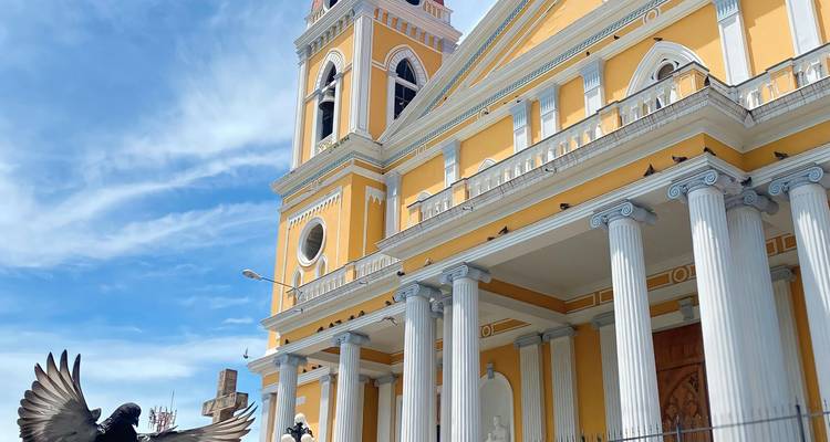 Heldergele kathedraal met witte zuilen en hoge klokkentoren onder een heldere blauwe hemel.