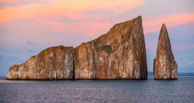 Dramatische Zwillingstürme des Kicker Rock, die bei Sonnenuntergang mit pastellfarbenem Himmel aus dem Meer ragen.
