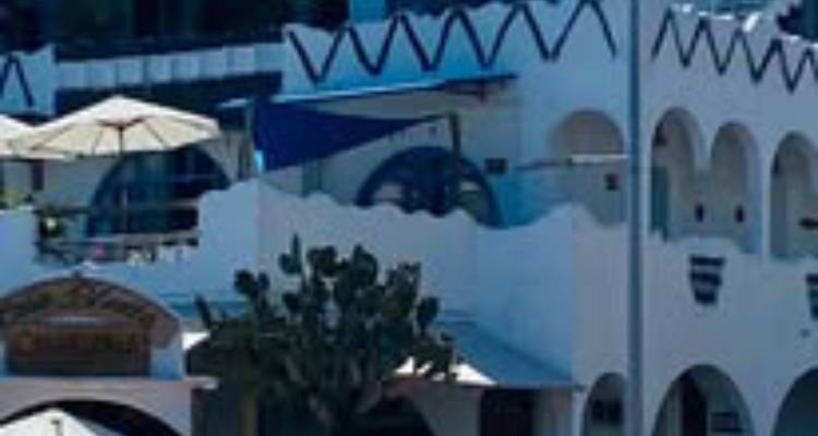 Nahaufnahme eines weiß getünchten Gebäudes mit blauen Verzierungen und einem Sonnenschirm im Freien, aber das Bild ist weich und pixelig.