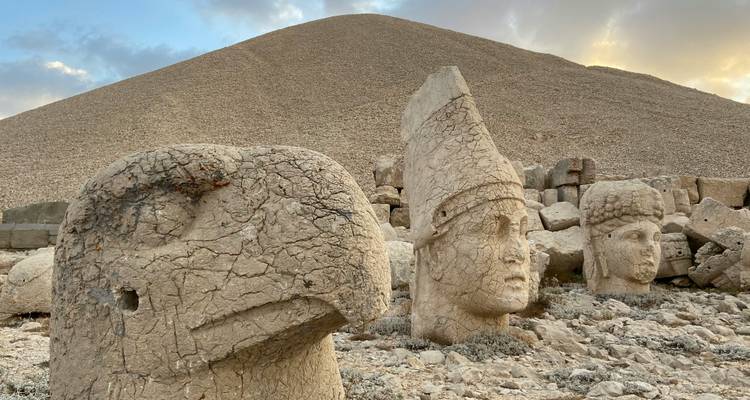 Têtes de pierre patinées d'anciennes divinités au pied du mont Nemrut sous un ciel dramatique.