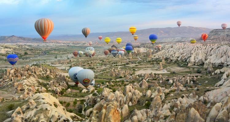 Des dizaines de montgolfières colorées flottent au-dessus des formations rocheuses uniques de la Cappadoce au lever du soleil.