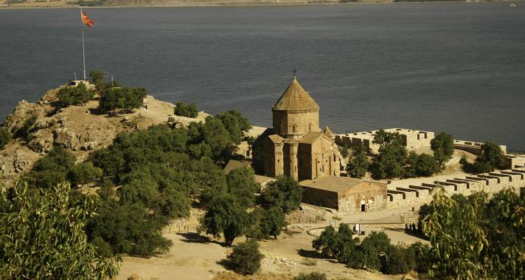 Ancienne église de pierre sur une petite île entourée d'un lac bleu profond et de collines arides.
