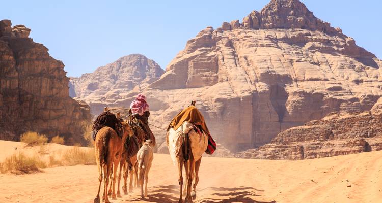 Beduinische Führer leiten Kamele durch die hoch aufragenden Sandsteinfelsen des Wadi Rum.