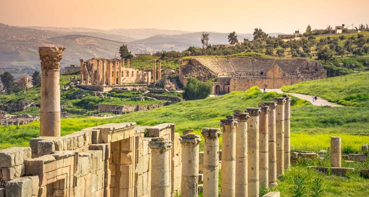 Sonnendurchflutete römische Säulen und Theaterruinen inmitten sanfter grüner Hügel in Jerash.