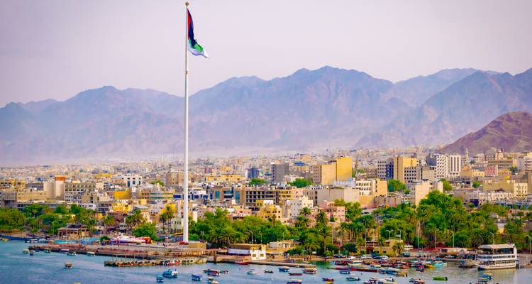 Panoramablick auf eine Küstenstadt mit einem riesigen nationalen Fahnenmast vor fernen Bergen.