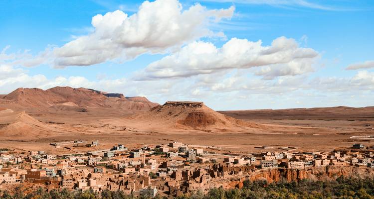 Panoramic view over desert village and flat-topped mesa under scattered clouds in Ouarzazate region.