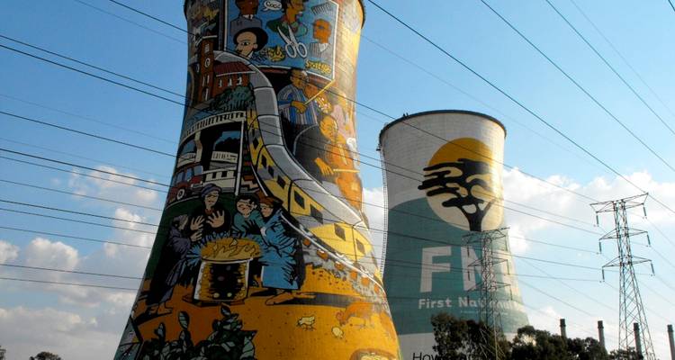 Colorfully painted twin cooling towers with murals, electric lines and blue sky.