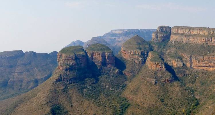 Rugged mountain escarpment with layered sandstone cliffs and hazy distant peaks.