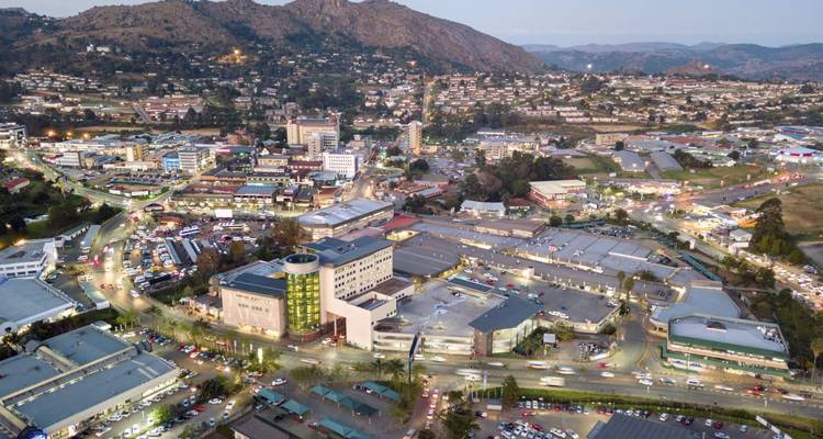 Evening aerial of a hilly city with clusters of buildings and winding roads lit by car lights.