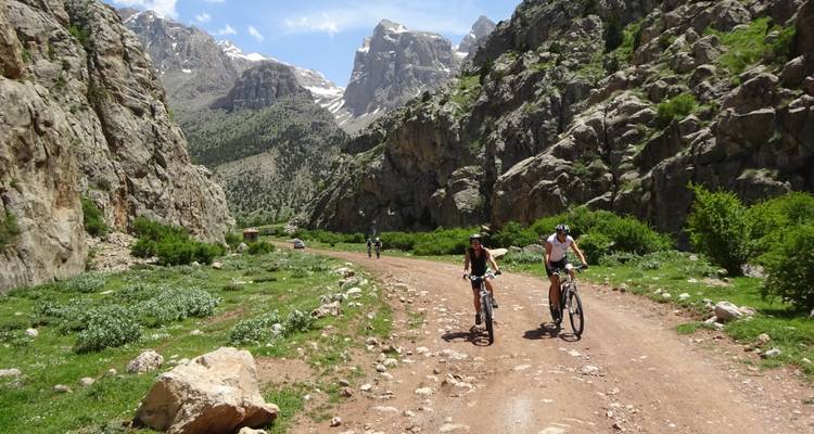 Des vététistes pédalant le long d'un chemin de terre accidenté bordé de pics rocheux spectaculaires et de verdure.