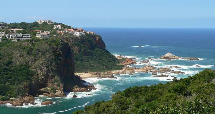 Rocky coastal cliff with upscale houses overlooking crashing teal waves.