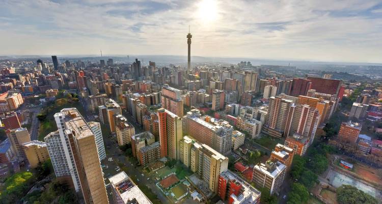 High aerial view over a dense downtown skyline with a tall communications tower piercing the hazy sky.