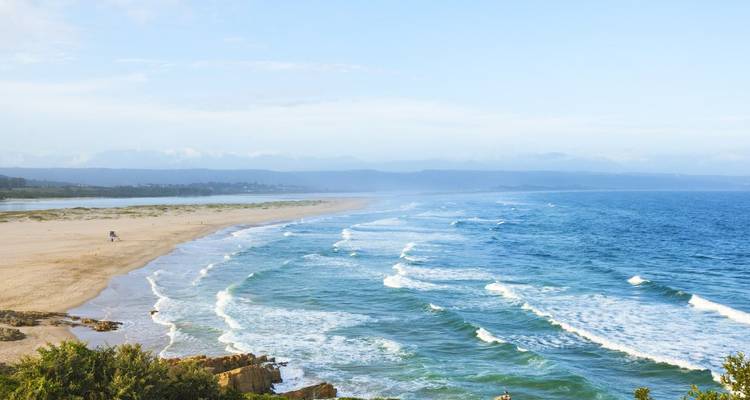 Long stretch of sandy shoreline with gentle waves and distant mountains under soft light.