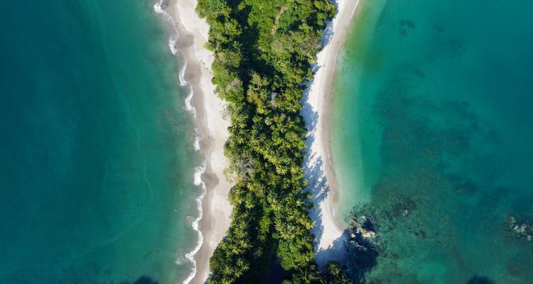 Vue de drone d'une étroite péninsule de jungle divisant deux baies turquoise.
