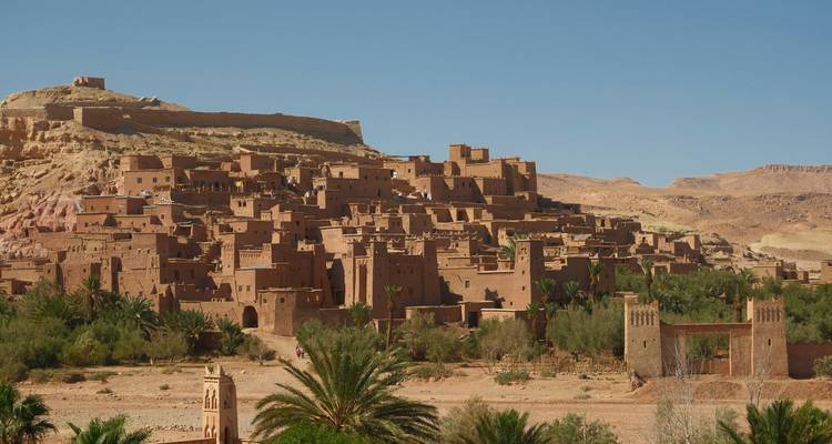 Clay-brick kasbah of Ait Benhaddou rises from the desert plain against blue sky.