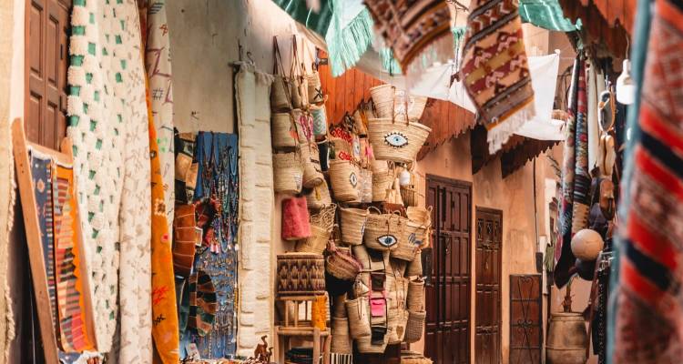 Ruelle étroite de marché marocain avec des tapis suspendus et des articles tissés.