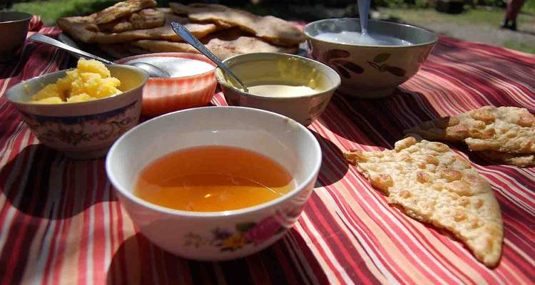 Close-up of traditional Kyrgyz breakfast spread featuring tea, breads and preserves on a striped cloth outdoors.
