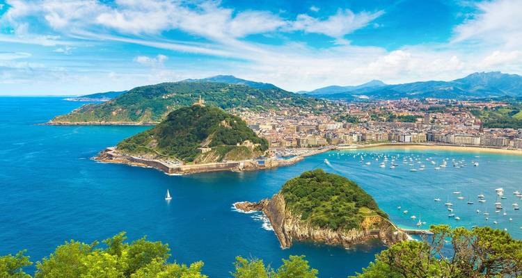 Vue panoramique sur la baie de Saint-Sébastien avec des collines verdoyantes, des plages de sable et une eau bleue scintillante.