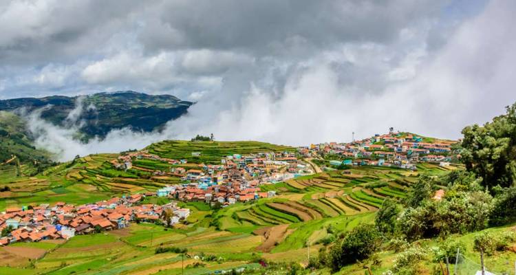 Panoramic view of colourful hill village and terraced fields under dramatic clouds in the Nilgiri Hills.