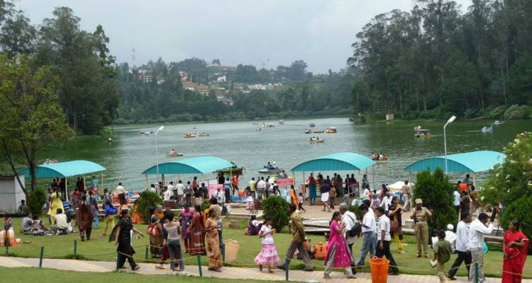 Crowds enjoy paddle boating and lakeside activities at a popular green hill station lake.
