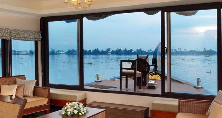 Elegant lounge of a Kerala houseboat with panoramic windows overlooking tranquil backwaters.