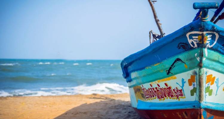 Ein bunt bemaltes Fischerboot ruht an einem Sandstrand und blickt auf sanfte blaue Wellen.