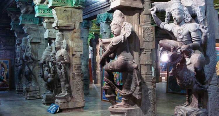 Kunstreich geschnitzte Steinstatuen säumen die Säulen einer südindischen Tempelhalle und zeigen detailreiche hinduistische Gottheiten im gedämpften Innenlicht.