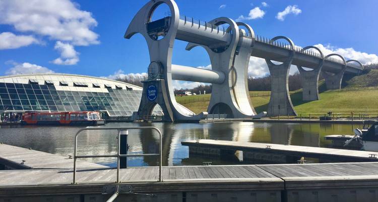 The modern Falkirk Wheel boat lift spanning a canal above a reflective basin under blue skies.