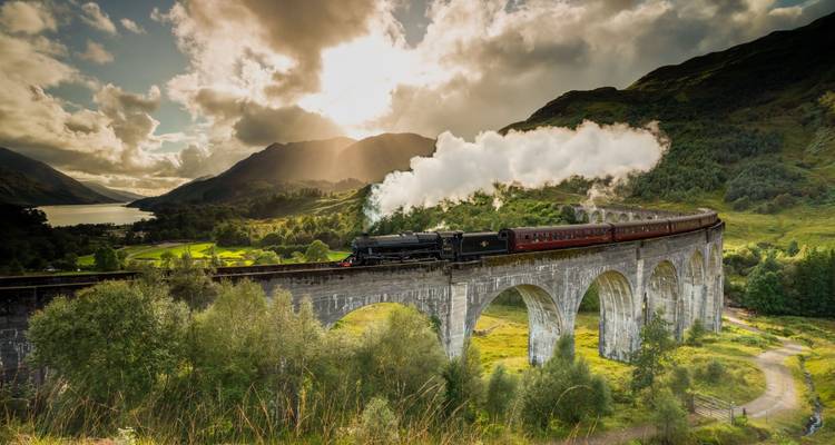 Steam locomotive crossing the Glenfinnan Viaduct amid dramatic highland scenery after rainfall.