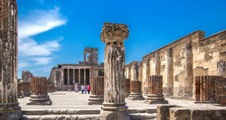 Ruined columns and temples of Pompeii's ancient forum under a vivid blue sky.
