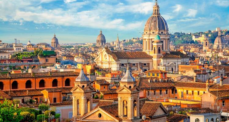 Panoramic skyline of Rome featuring domes, towers and terracotta rooftops at golden hour.