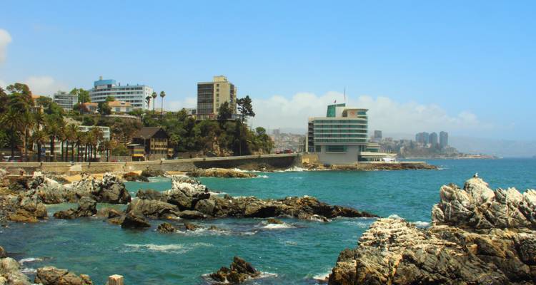 Rocky Pacific coastline with turquoise waters and modern seaside buildings under a clear sky.