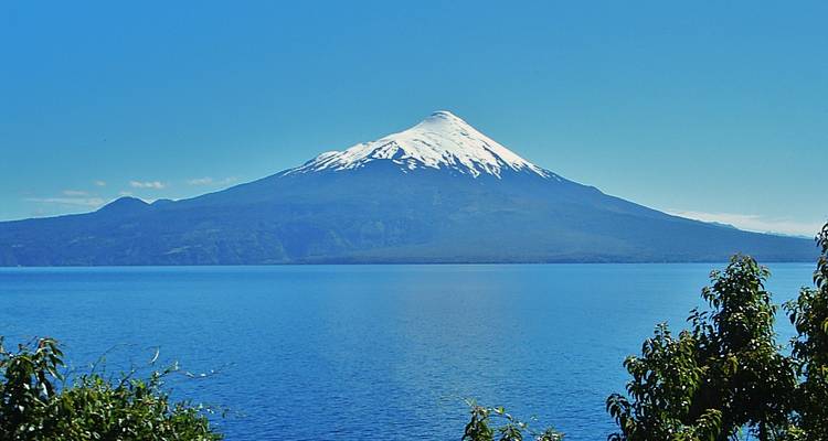 Snow-capped conical volcano towering above a vast blue lake on a clear day.