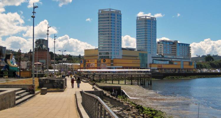 Urban waterfront promenade with modern high-rise towers beside a wide tidal estuary.