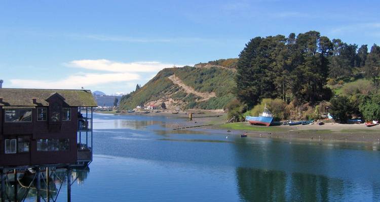 Calm inlet with forested hillsides, small boats beached on the shore and blue skies overhead.