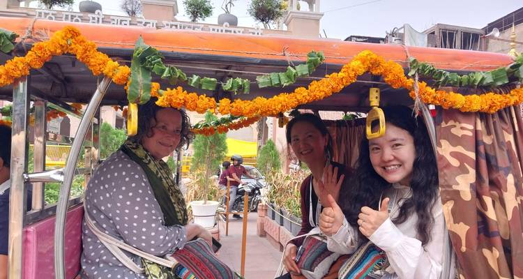 Smiling travelers give thumbs up while seated in a decorated tuk-tuk festooned with marigolds.