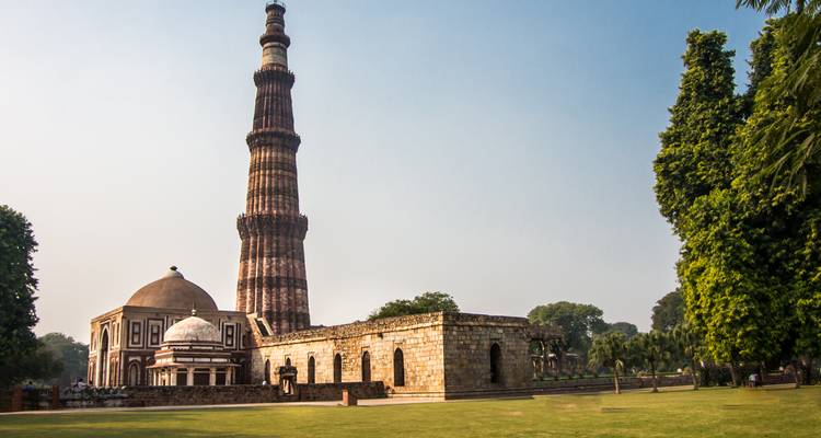 Historic Qutub Minar minaret rises beside ancient mosque structures on a clear day.