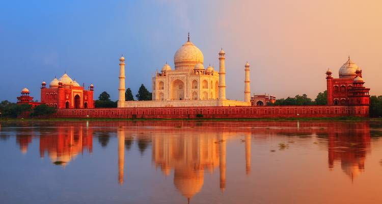 Taj Mahal reflected in the Yamuna River under soft sunrise light with pastel sky.