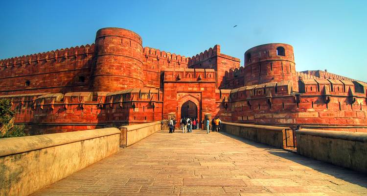 Visitors walk over the sandstone bridge toward imposing red Agra Fort walls.