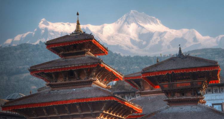 Traditional pagoda roofs of Kathmandu valley temple with snowy Himalayan peak beyond.